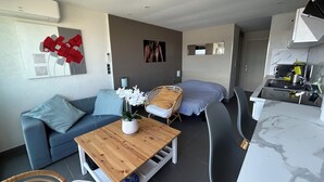 A modern living space with a sofa, a wooden coffee table, a dining area with a chair, a kitchen with a sink, and a bed. - Naturiste Cap d'Agde Port Vénus 212 (Agde)