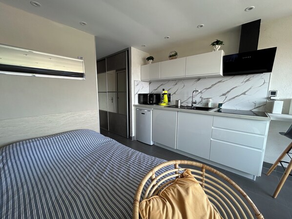 Una habitación de hotel compacta con cama, kitchenette pequeña, zona de comedor y baño.