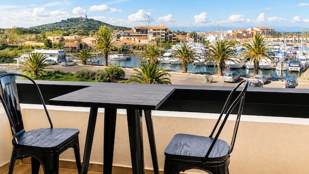 Un balcón con dos sillas y una mesa que da a un puerto deportivo con barcos y edificios.