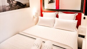 Habitación de hotel con una cama, almohadas, un espejo, un televisor montado en la pared y un cuadro en la pared.