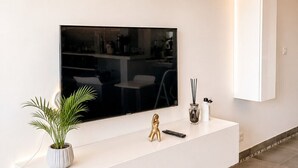 Una sala moderna con televisor de pantalla plana, muebles blancos, una planta en maceta y una figura decorativa dorada.