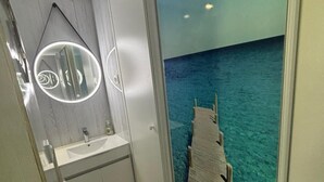Een badkamer met een modern design, met een witte wastafel en spiegel, en uitzicht op de oceaan door een groot raam.