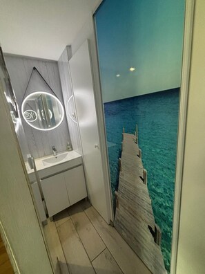 A bathroom with a modern design, featuring a white sink and mirror, and a view of the ocean through a large window.