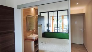 A modern bedroom with a bed, a built-in wardrobe, a bathroom with a mirror and sink, and a view of the outdoors through a large window. - Naturiste Cap d'Agde Port Nature 827 ** (Agde)