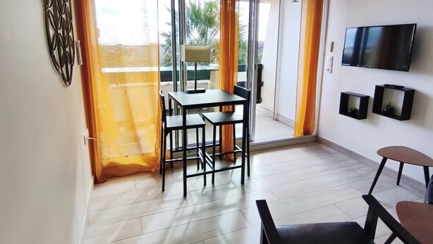 A modern living room with a dining area, a TV mounted on the wall, and a balcony with curtains. - Naturiste Cap d'Agde Port Nature 827 ** (Agde)