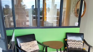 A room with a green wall, two black leather chairs with patterned cushions, a small wooden table, and a large window with a view of the outside. - Naturiste Cap d'Agde Port Nature 827 ** (Agde)
