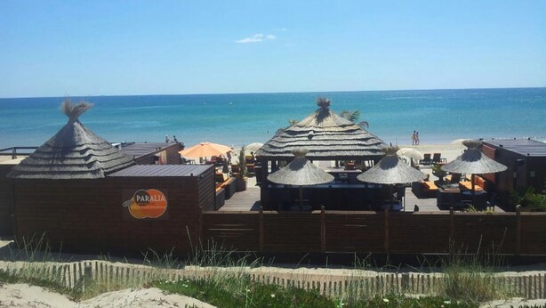 A beachside resort with thatched-roof structures, outdoor seating, and a view of the ocean. - Naturiste Cap d'Agde Héliopolis AB 30 (Agde)
