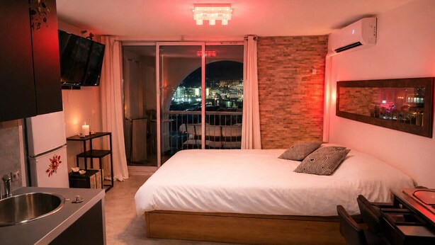 Ein Hotelzimmer mit Bett, Schreibtisch, Fernseher und einem Balkon mit Blick auf die Stadt, inklusive Klimaanlage.