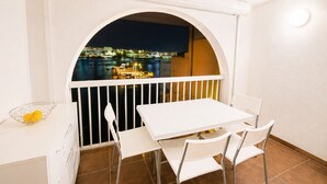 Ein Balkon mit weißem Tisch und Stühlen, einem weißen Geländer und Blick auf eine nächtliche Skyline.