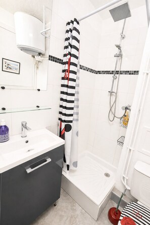 Um banheiro com chuveiro, vaso sanitário, pia com dosador de sabonete e porta-toalhas.