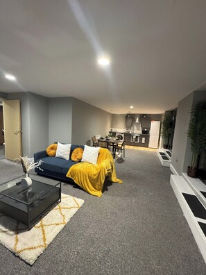 A modern living room with a sofa, coffee table, and a dining area in the background. - Modern 2 Bedroom City Oasis in Manchester (Manchester)