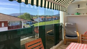 A balcony with a striped awning, a table with a checkered tablecloth, and a chair. - Résidence Eihera BuildingB (Hendaye)