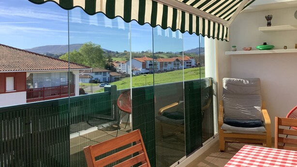 A balcony with a striped awning, a table with a checkered tablecloth, and a chair. - Résidence Eihera BuildingB (Hendaye)