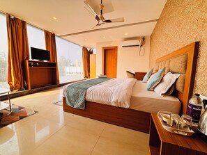 A modern hotel room with a large bed, a flat-screen TV, a ceiling fan, and a view of the city. - Aqoss Hotel (Patna)