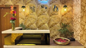 A reception area with a wooden reception desk, a number sign '305', framed artwork on the wall, and a flower vase. - Aqoss Hotel (Patna)