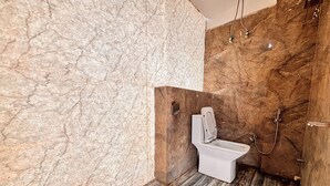 A modern bathroom with a marble wall, a toilet, and a shower area. - Aqoss Hotel (Patna)