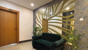 A room with a green sofa, a wooden door labeled '301', a decorative wall with a tree design, and a potted plant. - Aqoss Hotel (Patna)