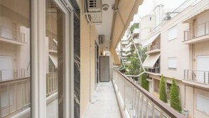 A narrow balcony with a glass railing, a tiled floor, and a view of adjacent buildings. - Cozy home in Athens (Nea Smirni)