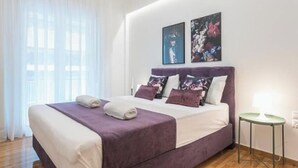 A bedroom with a bed, pillows, a bedside table, and artwork on the wall. - Cozy home in Athens (Nea Smirni)