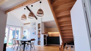 A spacious interior with a wooden ceiling, a dining area with chairs and a table, and a kitchen with wooden cabinets.