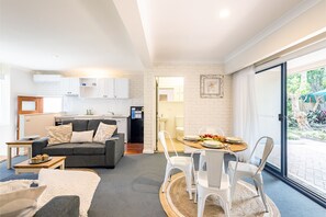 Een compacte leefruimte met een kitchenette, een eethoek en een zithoek met een bank en stoelen.