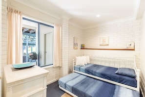 Een slaapkamer met een witte baksteenmuur, een bed met blauw beddengoed, een witte dressoir en een raam met gordijnen.
