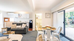 Relax in a cozy living area with a sofa, coffee table, and dining table for four, plus a balcony with a garden view.