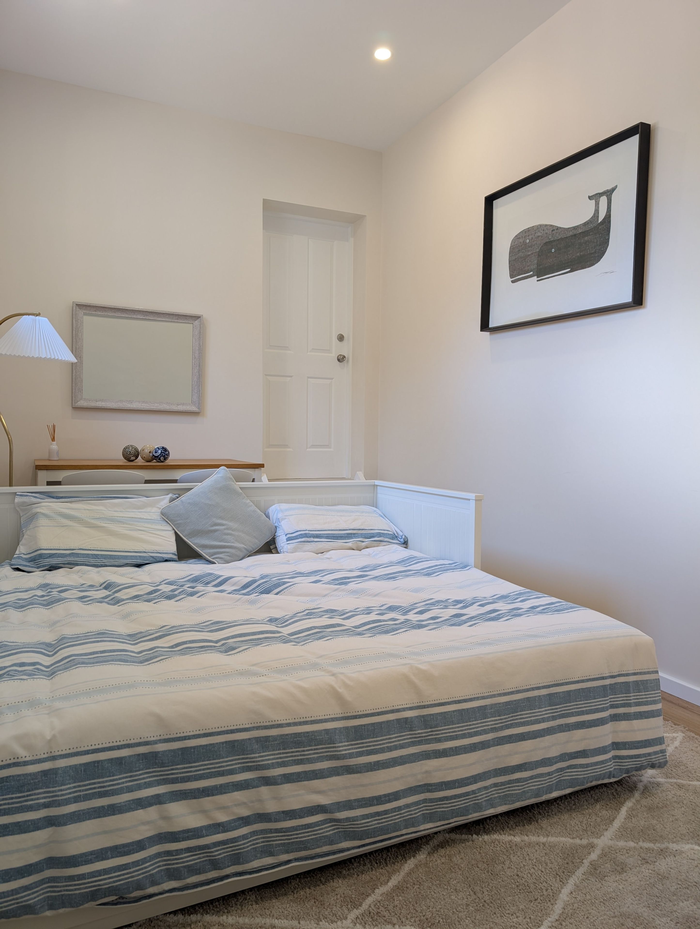 A bedroom with a bed, a door, a framed picture on the wall, and a lamp.
