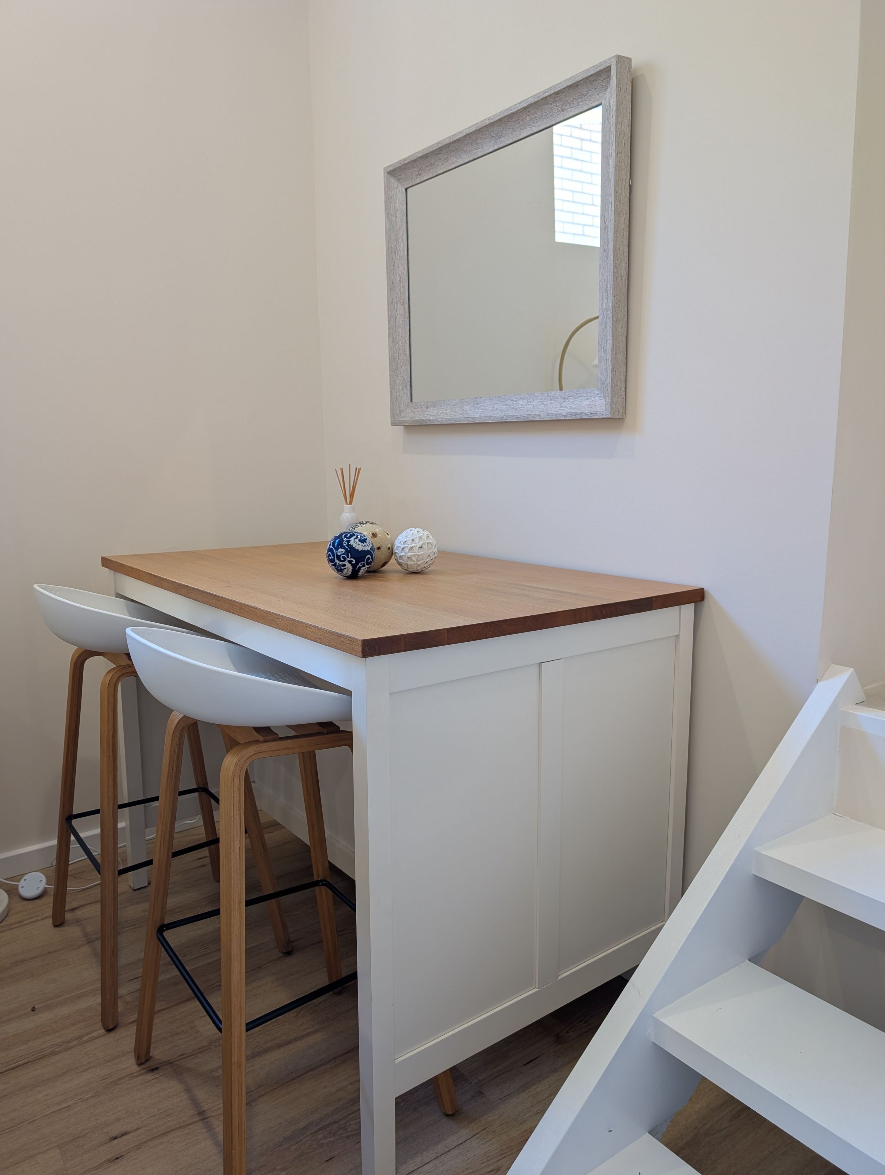 A small kitchenette with a white cabinet, a wooden countertop, and two white bar stools.