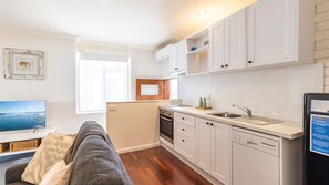 Enjoy cooking in the well-equipped kitchen with oven and dishwasher, adjacent to a cozy living area with a sofa and TV.