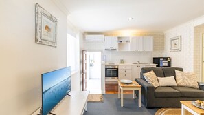 Cozy living space with a flat-screen TV, sofa, and kitchenette featuring a stove and oven.