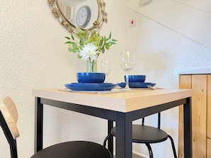 Mesa de jantar com louça azul e um vaso de flores, em frente a uma parede texturizada com um relógio.