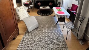 Una sala de estar con sofá, alfombra estampada, mesa de comedor con mantel blanco y chimenea.
