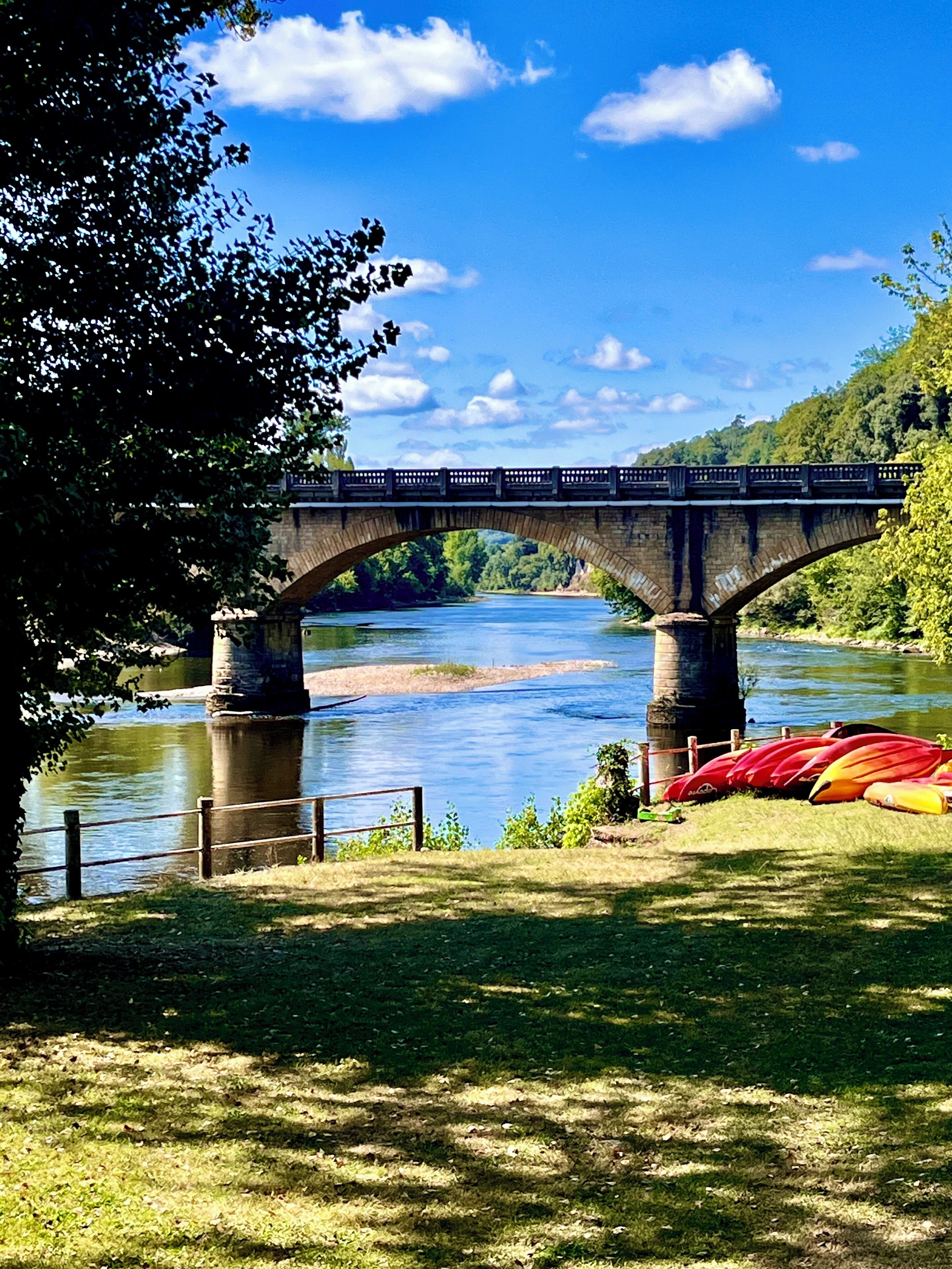 A stone bridge over a river with kayaks on the shore.
