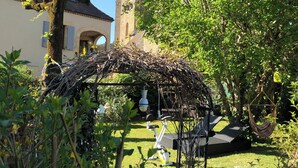 Un jardín con una pérgola, una mesa con sillas y un sillón colgante.