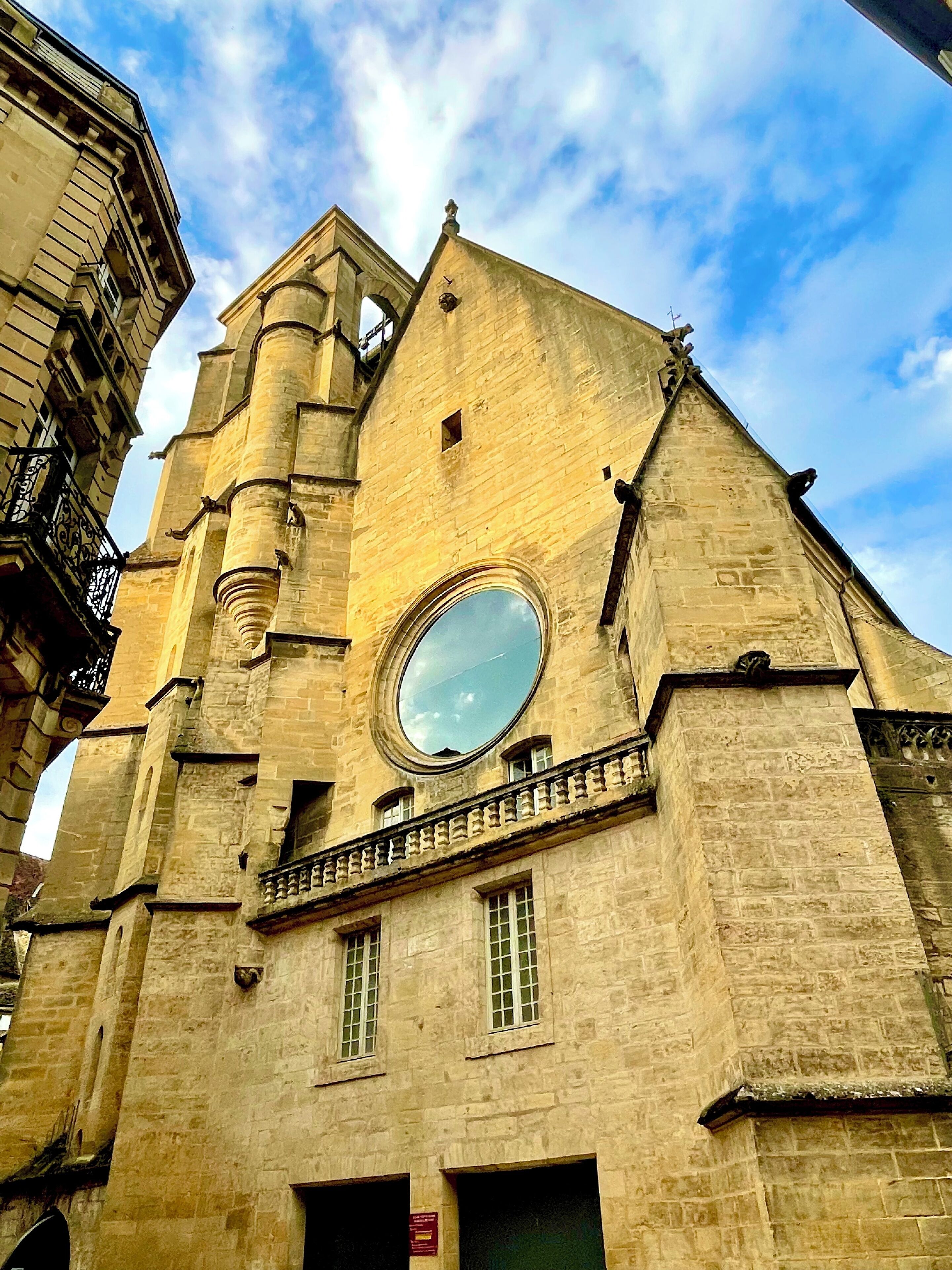 Un edificio histórico de piedra con un gran ventanal circular, un balcón y una torre de reloj.