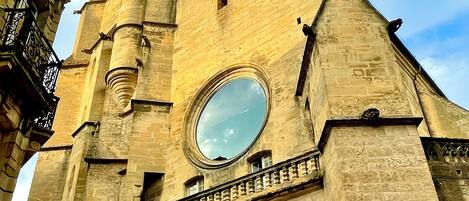 Un edificio histórico de piedra con un gran ventanal circular, un balcón y una torre de reloj.