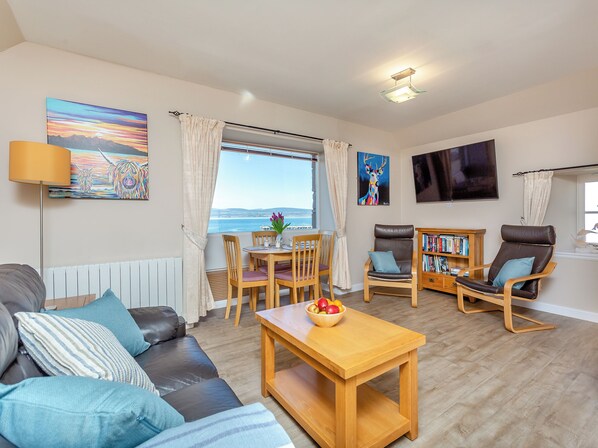 A living room with a sofa, chairs, a table with fruit, a bookshelf, and a painting of a deer.