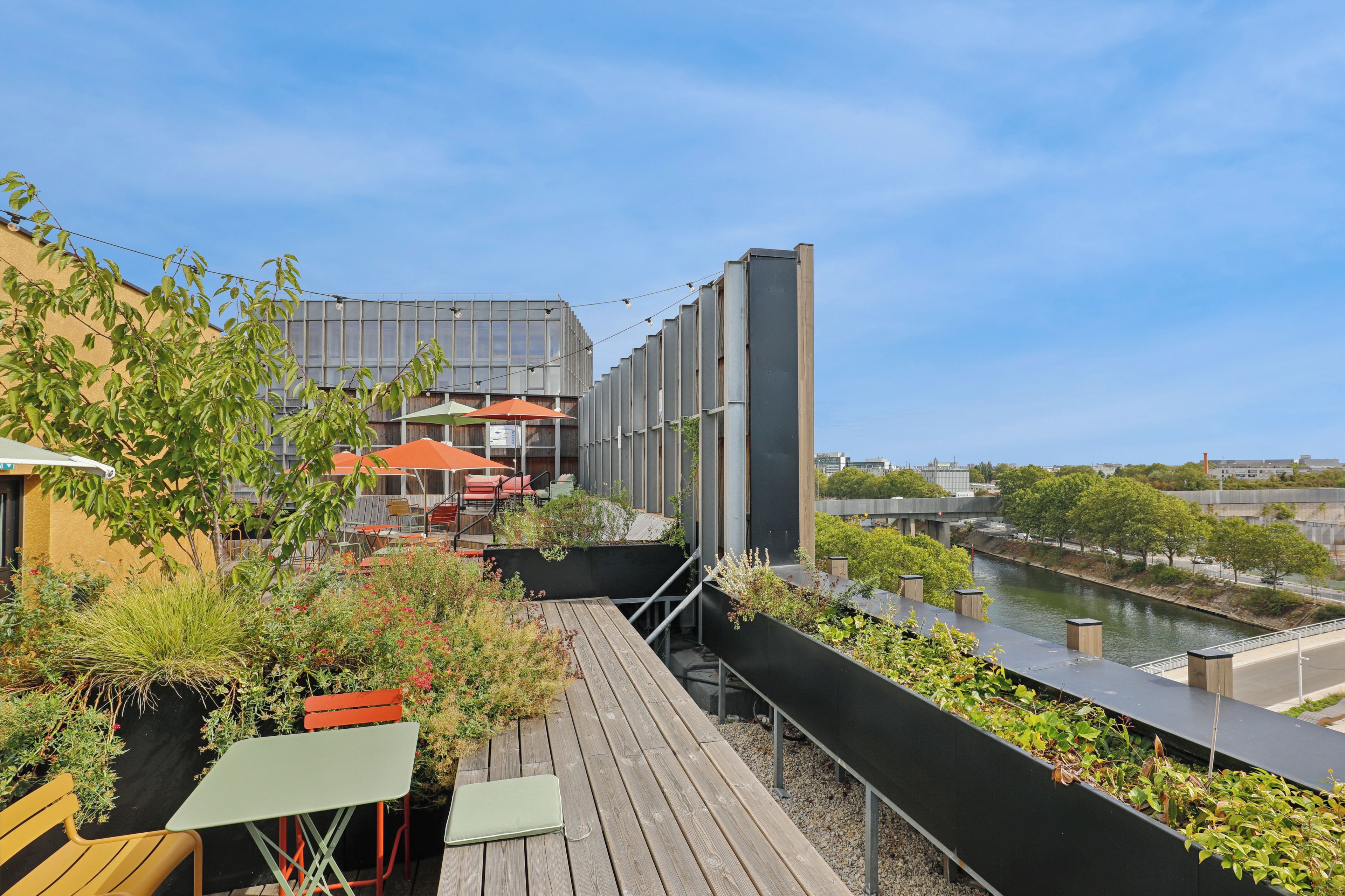Una terraza en la azotea con mobiliario exterior, vista a un río y un edificio moderno al fondo.