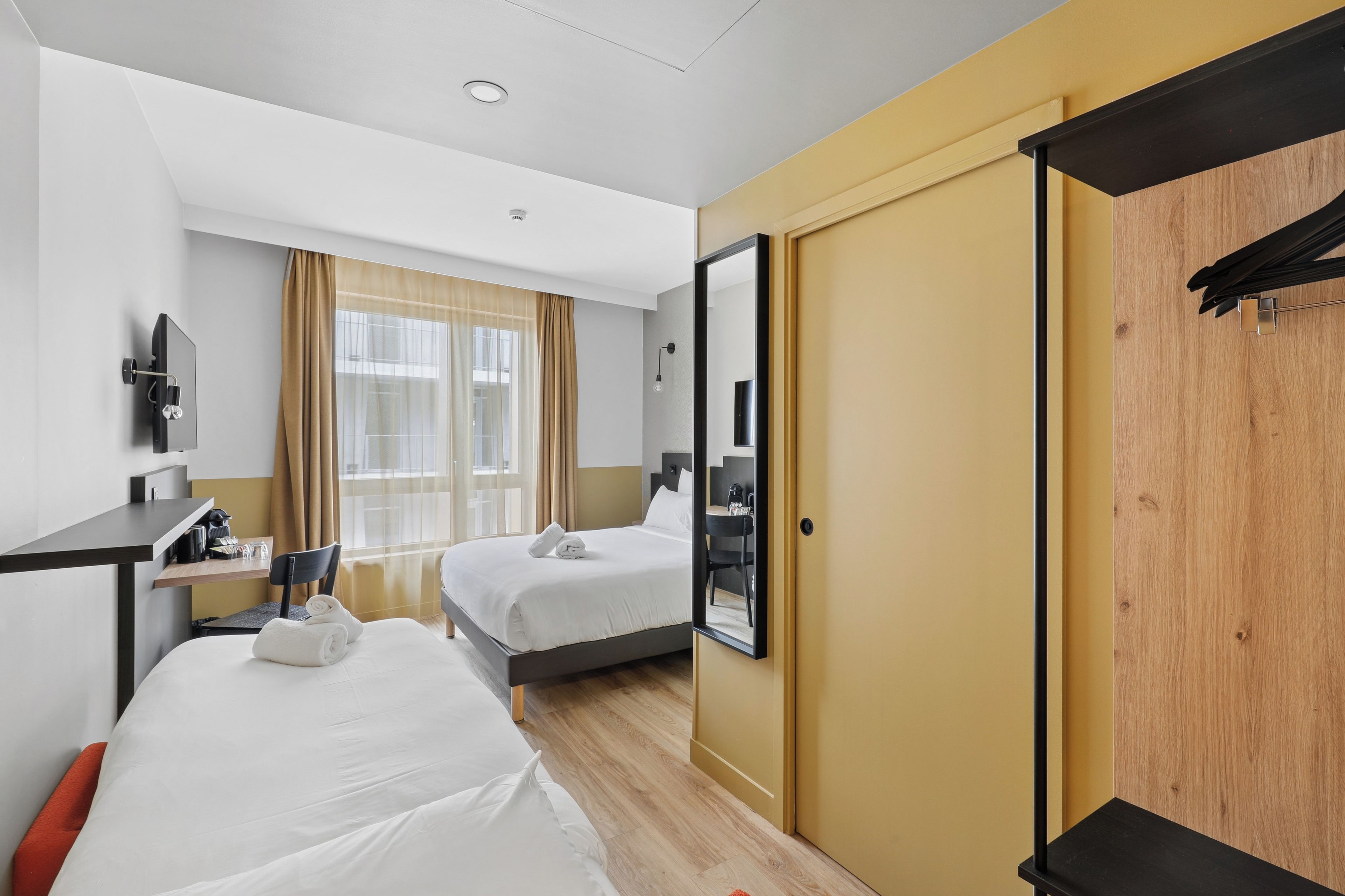 Une chambre d’hôtel avec deux lits, un bureau, une chaise, une armoire et un grand miroir.