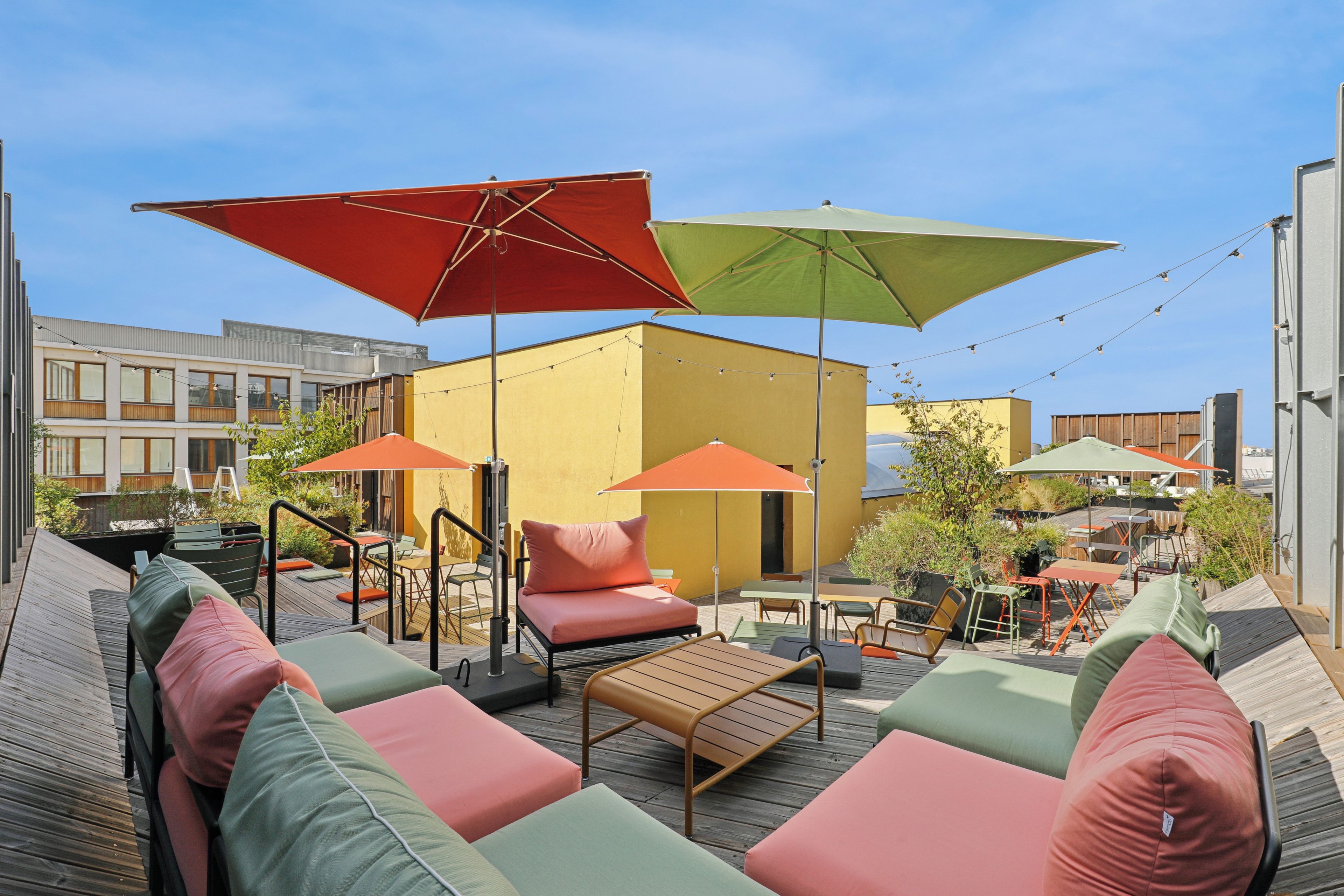 Un área de estar exterior con varias mesas y sillas, sombrillas y una terraza de madera.