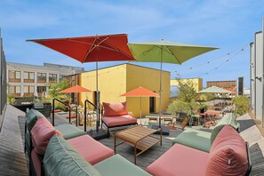 An outdoor seating area with multiple tables and chairs, umbrellas, and a wooden deck. - All Suites Hôtel | Paris Pleyel – L’île Saint Denis (L'Île-Saint-Denis)