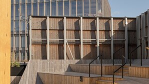 Un terrazza in legno con scale che conducono a un edificio moderno con ampie finestre.