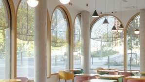Un interno ristorante moderno con ampie finestre ad arco, diversi tavoli e sedie, e lampade a sospensione.