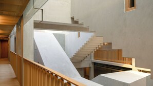 Un interno moderno con una scala che conduce a un piano superiore, una ringhiera in legno e un muro in cemento.