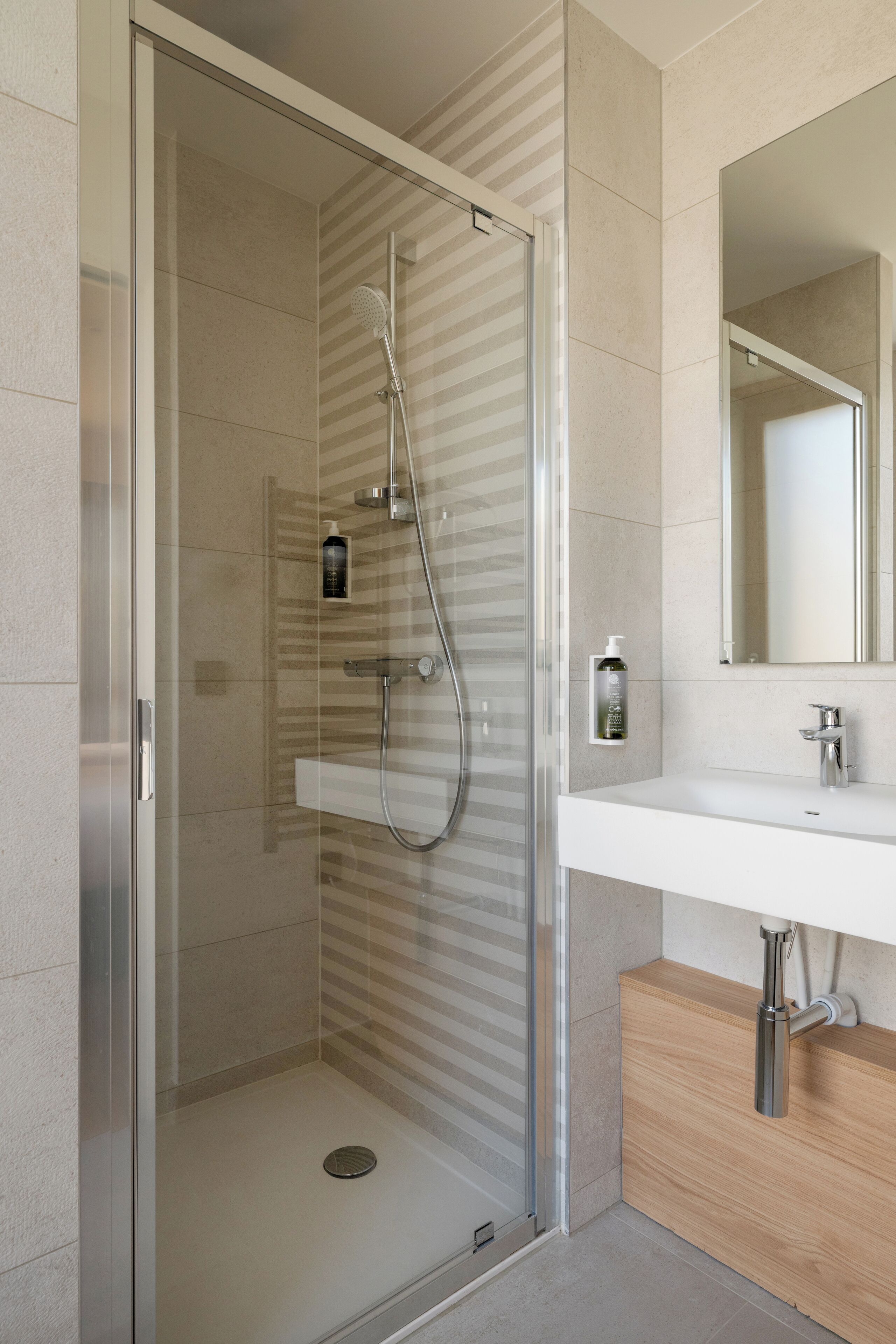 Ein modernes Badezimmer mit einer gläsernen Duschkabine, einem weißen Waschbecken und einem Holzkabinet.