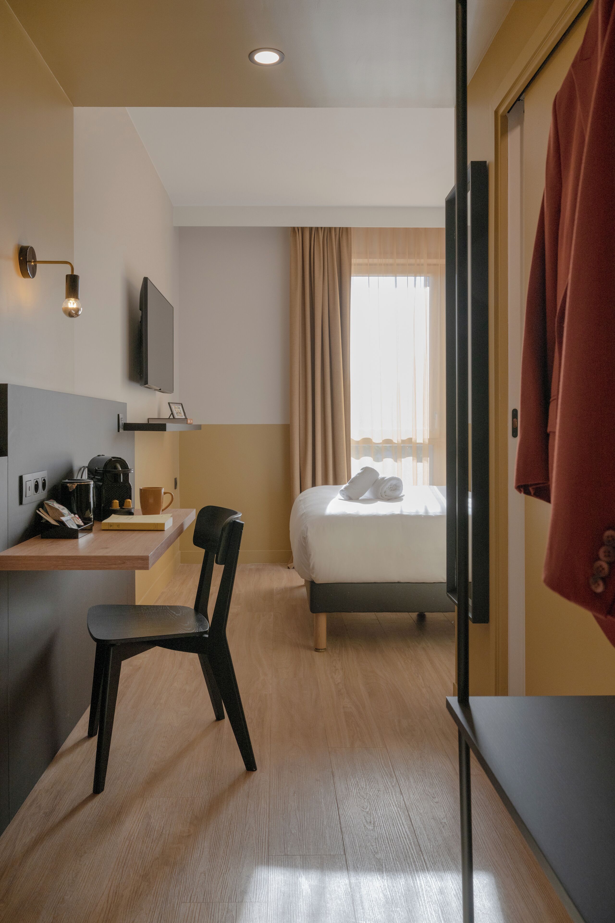 Habitación de hotel con cama, escritorio con silla, televisor y ventana con cortinas.