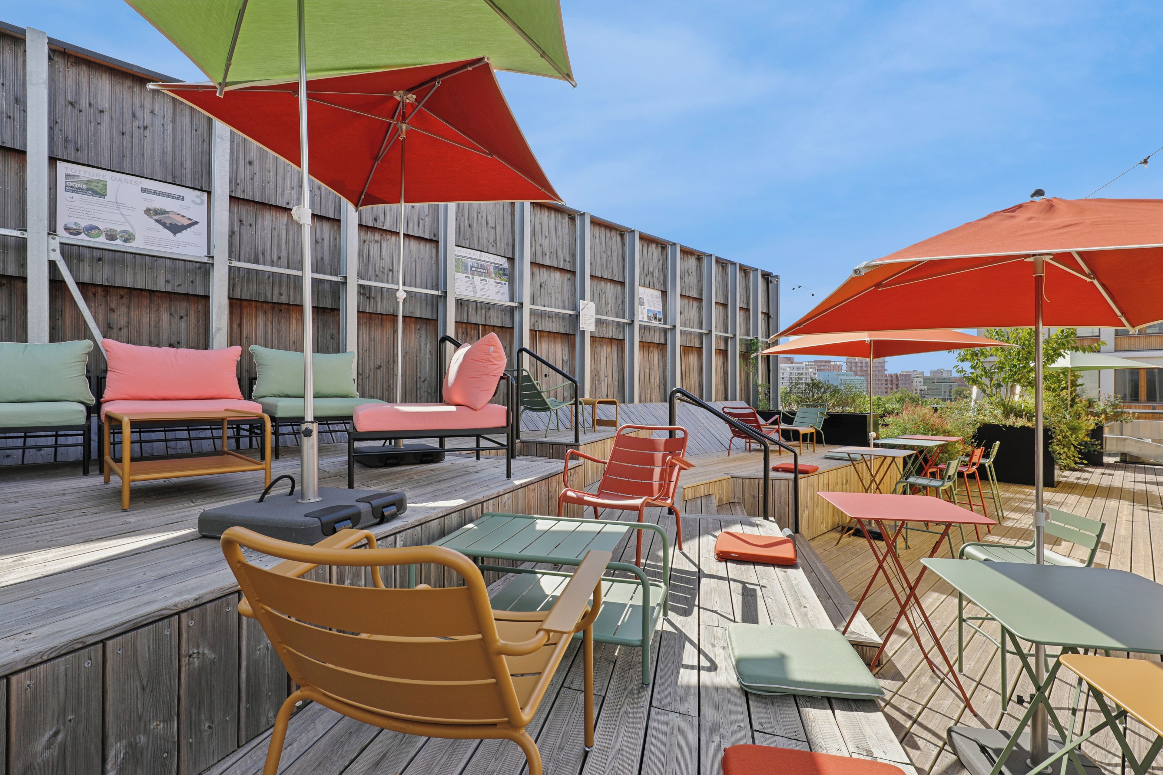 Un espace extérieur aménagé avec plusieurs tables et chaises, dont certaines sont dotées de parasols, ainsi qu’une terrasse en bois.
