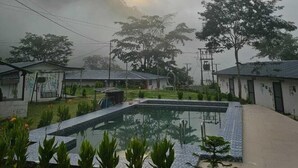 A swimming pool surrounded by greenery and buildings with a cloudy sky above. - The Himaya's resort  (Rishikesh)