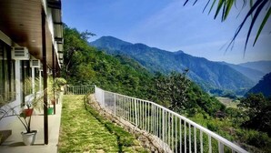 A balcony with a white railing overlooking a lush green landscape and mountains. - The Himaya's resort  (Rishikesh)